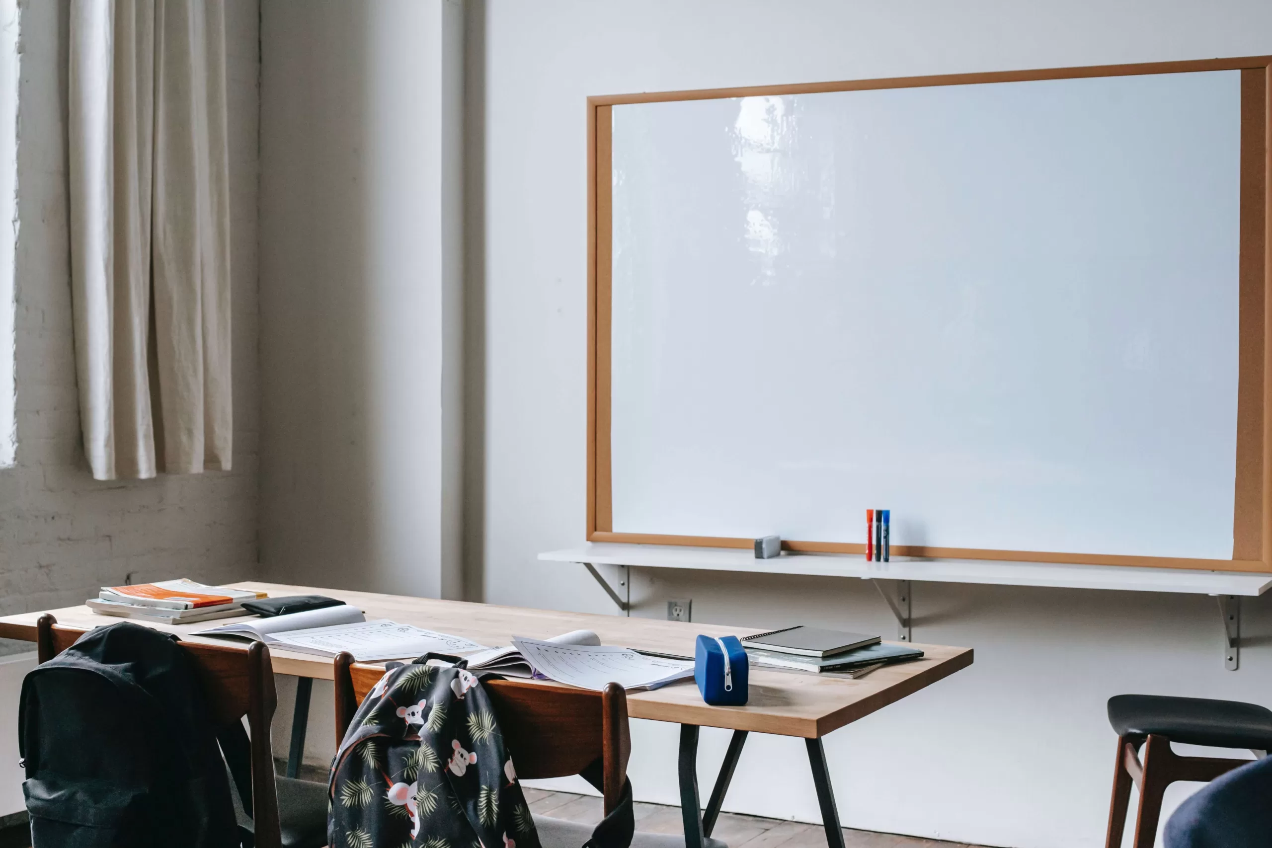 A school room with its desks, the teacher's desk, and the blackboard in white.